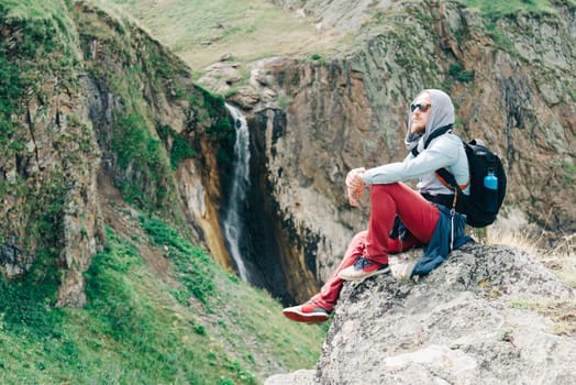 Traveler young man resting near the waterfall in summer mountains.