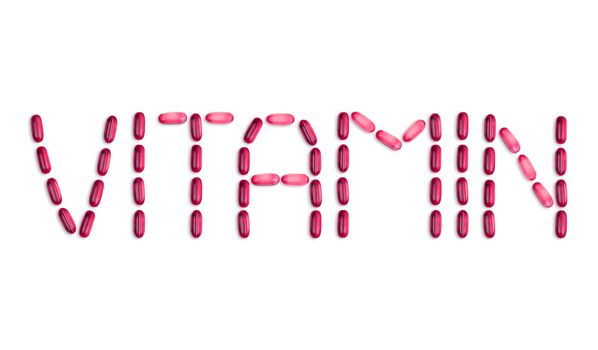 The word Vitamin is laid out with pills. The word Vitamin is laid out with gel pills on a white background with copy space for text.