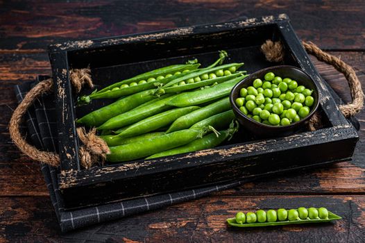 Raw green pea pods in a wooden tray. Dark wooden background. Top view.