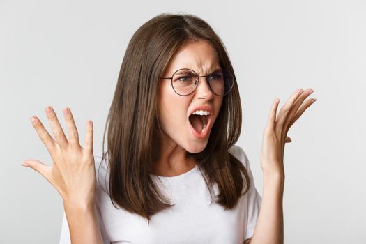 Close-up of angry and outraged beautiful woman in glasses yelling and shaking hands, having an argument.