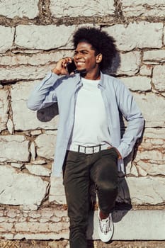 young african man with afro talking on mobile phone leaning on wall