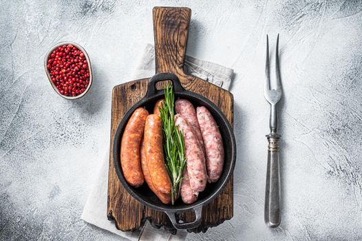 Assorted Raw sausages Chorizo and Bratwurst with spices in a pan with rosemary. White background. Top View.