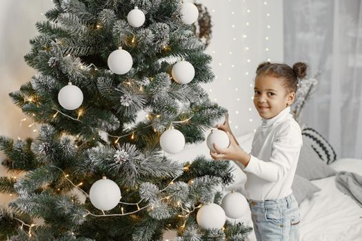 Child in a white sweater. Daughter standing near Christmas tree.