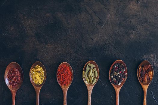 Various spices in wooden spoons on old black table