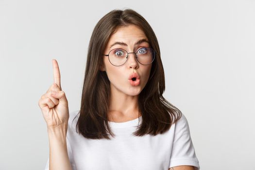 Close-up of smart cute girl in glasses raising finger eureka gesture, think-up idea.