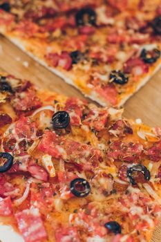 Fresh pizza with olives, cheese and bacon on kitchen table closeup