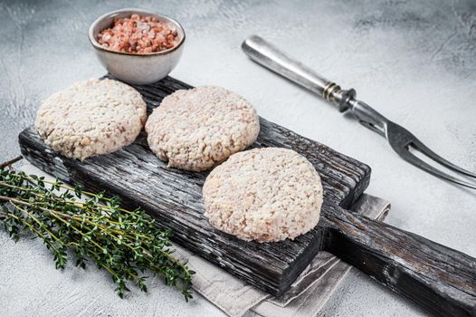 Raw meat patty cutlets with breadcrumbs on wooden cutting board. White background. Top view.