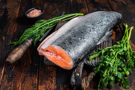 Big piece of Raw cut salmon fish on a wooden cutting board with chef knife. Dark Wooden background. Top view.
