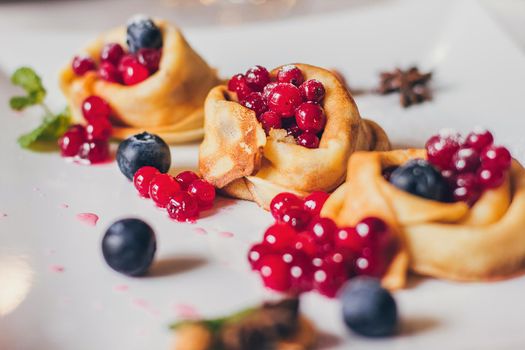 Plate of pancakes dripping with caramel with cranberries and blueberries, cinnamon sticks. Shrovetide Maslenitsa Butter Week festival meal. Shrove Tuesday. Pancake day.