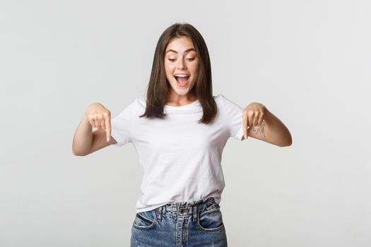 Excited happy brunette girl, looking and pointing down with amused smile.