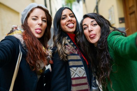 Multiethnic group of woman taking a selfie photo sticking out their tongues outdoors
