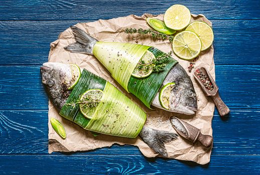 two fresh raw dorado fish, wrapped in palm leaves, sprinkled with a mixture of peppers and large gimolais salt, with slices of lime and lemon, ready to be baked. cooking dinner concept for two