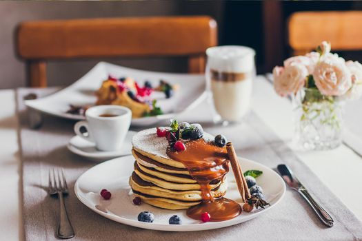 Plate of pancakes dripping with caramel with cranberries and blueberries. Shrovetide Maslenitsa Butter Week festival meal. Shrove Tuesday. Pancake day.