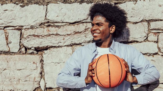 Young afro man with basket ball over stone wall, copy space