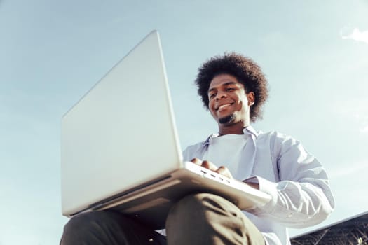 close up from below of young african student working in laptop outdoors