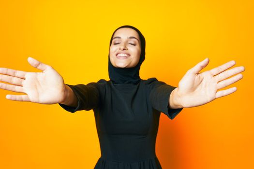 Muslim in black hijab posing fashion hand gesture yellow background. High quality photo