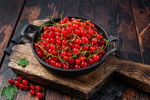 Red currant berries in a pan. Dark wooden background. Top view.