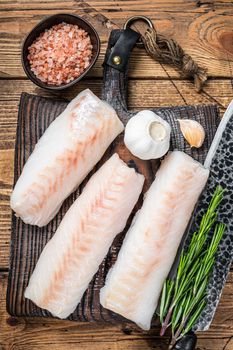 Fresh Raw cod loin fillet steaks on wooden board with butcher knife. wooden background. Top view.