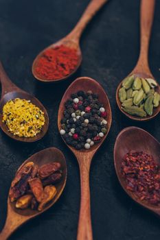 Various spices in wooden spoons on old black table