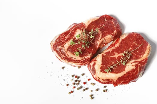 two fresh marbled beef steaks on a white plate with a sprig of rosemary, salt and different varieties of peppers