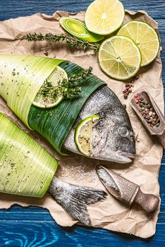 two fresh raw dorado fish, wrapped in palm leaves, sprinkled with a mixture of peppers and large gimolais salt, with slices of lime and lemon, ready to be baked. cooking dinner concept for two