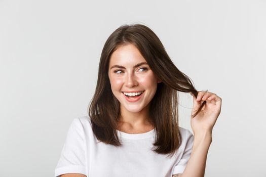 Close-up of flirty attractive brunette girl playing with hair strand, smiling and looking intrigued to the right.