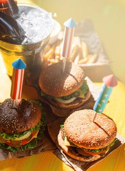 three fresh and juicy burgers with American flag-style fireworks inserted into them. bbq concept picnic to celebrate independence day