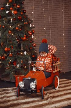 Cute little boy in a red sweater. Child by the christmas tree. Kid with toys car.