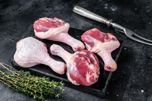 Uncooked Raw Duck legs drumsticks on marble board. Black background. Top view.