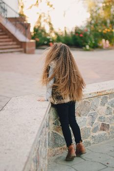 Stylish baby girl 4-5 year old wearing boots, fur coat with very long curly hair. View from the back. Autumn fall season.