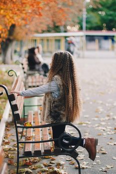 Stylish baby girl 4-5 year old wearing boots, fur coat with very long curly hair. View from the back. Autumn fall season.