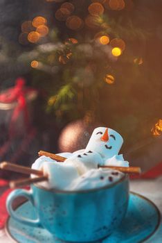 Christmas background with a marshmallow man lying in a mug with cocoa, in the background a Christmas tree with toys, a garland and gifts