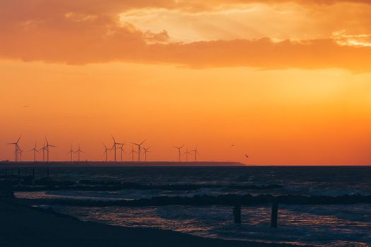 Wind turbine power generators silhouettes at ocean coastline at sunset. Alternative renewable energy production