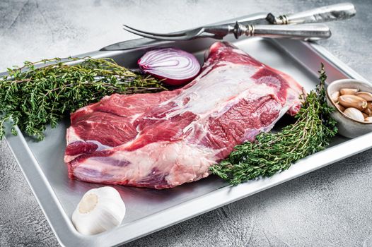 Raw lamb or goat shoulder meat in a baking dish with knife and meat fork. White background. Top view.