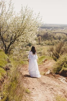 Portrait of carefree young woman in white vintage wedding style dress in spring cherry blossom garden valley.