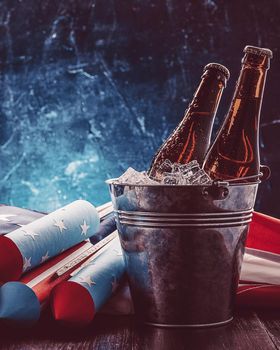 two bottles of beer in an ice bucket with the American flag lying nearby and rockets for fireworks. Independence Day celebration concept