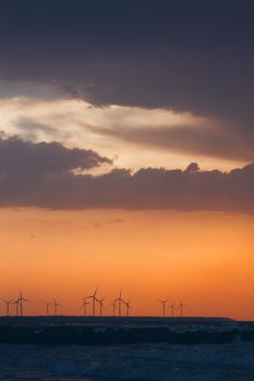 Wind turbine power generators silhouettes at ocean coastline at sunset. Alternative renewable energy production