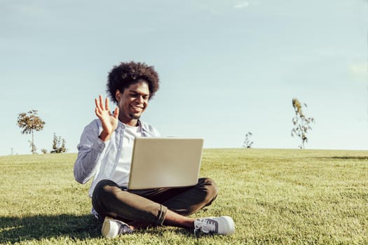 african american man with afro hair using his laptop sitting on the grass of an urban park