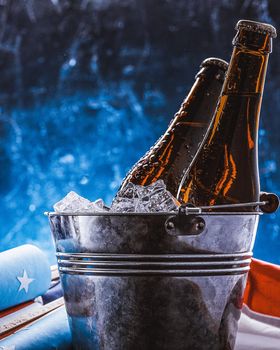 two bottles of beer in an ice bucket with the American flag lying nearby and rockets for fireworks. Independence Day celebration concept