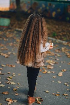Stylish baby girl 4-5 year old wearing boots, fur coat with very long curly hair. View from the back. Autumn fall season.