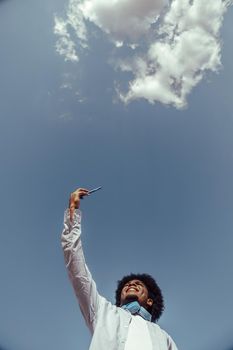 Young afro man taking selfie on sky background. View from below