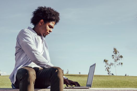 Side portrait of a smiling afro guy sitting outside with laptop