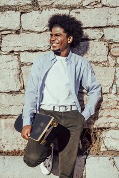 Portrait of smiling young african american man leaning on wall with skate