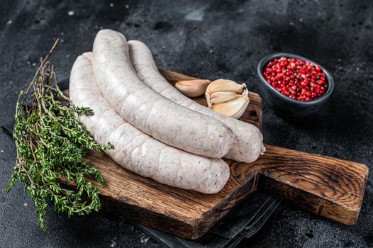 Raw Munich white sausage weisswurst on wooden board. Black background. Top view.