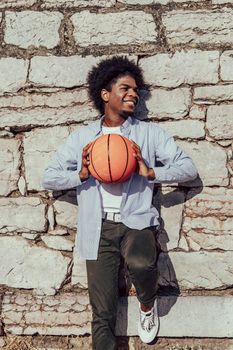 young american man with afro hair leaning on wall with basket ball