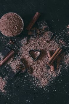 Chocolate bar pieces with cocoa powder and heart shape on dark background, cope space.