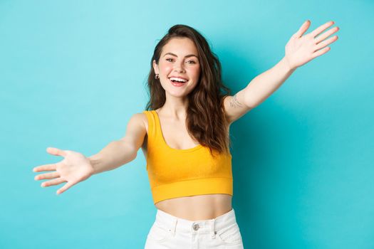 Summer and lifestyle concept. Attractive friendly woman stretch out hands and smiling happy, inviting you for hug, welcome or greet friend, standing over blue background.