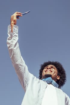 Vertical portrait of young african american man with afro hair taking selfie. View from below