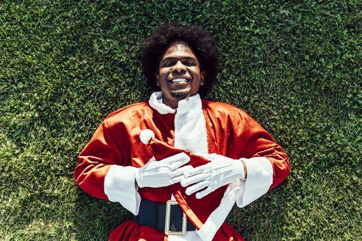 african american santa claus lying on the grass and smiling to the camera