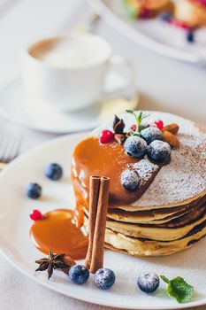 Plate of pancakes dripping with caramel with cranberries and blueberries, cinnamon sticks. Shrovetide Maslenitsa Butter Week festival meal. Shrove Tuesday. Pancake day.